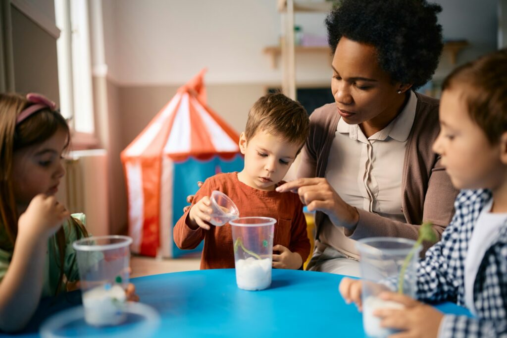 Black female teacher teaching group of kids to plant seeds at preschool.