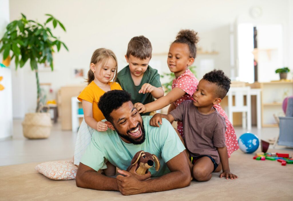 Nursery school children with man teacher sitting on floor indoors in classroom, playing.